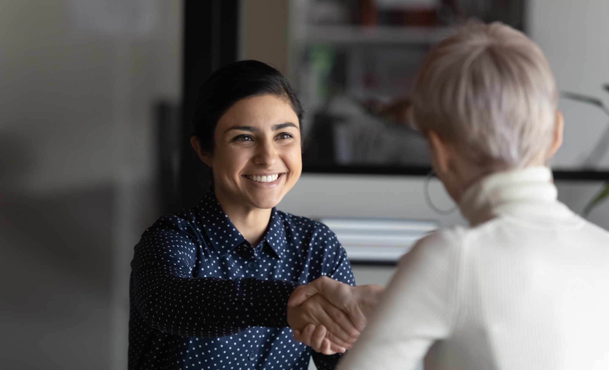 Smiling Indian woman shaking hands with older female boss